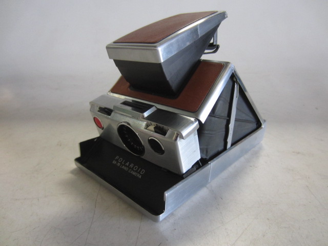 Polaroid SX-70 Land Camera, With Neck Strap. Uses Polaroid SX 70 film, readily available as of 04/23/2019.  Introduced: 1972, Tan, Polaroid, 1970s+, Metal, 1"H, 4"W, 7"L