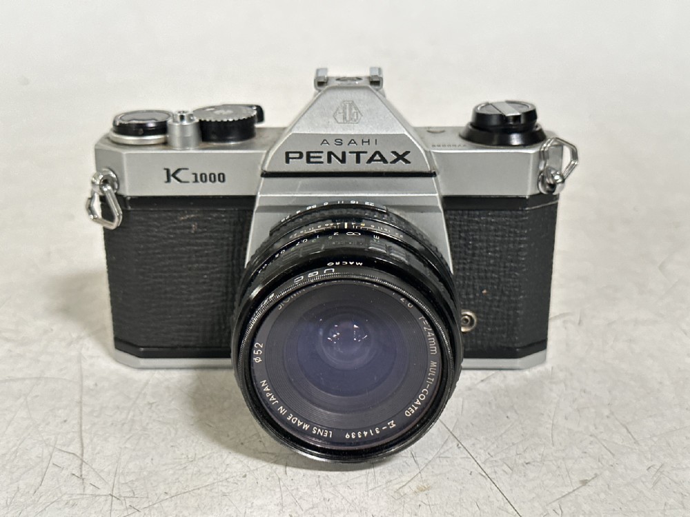 Camera, 35mm, Asahi Pentax Model K-1000, Serial Number 7760099, With Sigma Super-Wide 1:2.8 f=24mm Lens (Serial Number E-314399), Has Hot Shoe That Will Allow An Attached Flash Unit To Be Triggered By The Shutter Release When Camera Is Wound, Silver, Pentax, 1960s+, Metal
